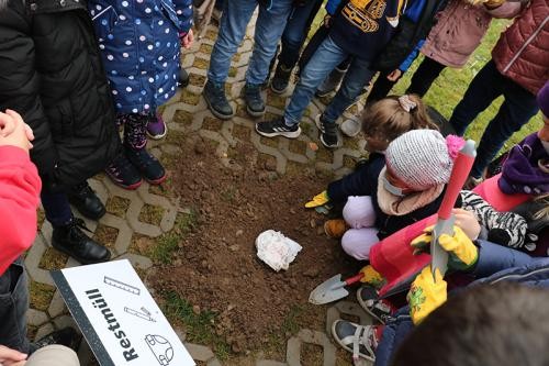 Kinder, die im Kreis um einen Abfall in der Erde stehen